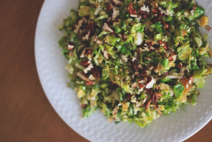 An overhead shot shows a warm brussels sprouts sauté with chopped pecans on top.