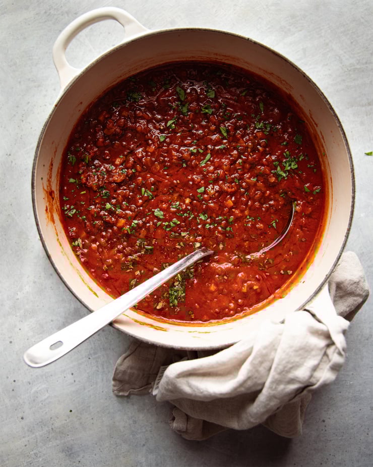 Image taken from overhead shows a pot of deep red soup with little green flecks of parsley. A ladle is sticking out of the pot.