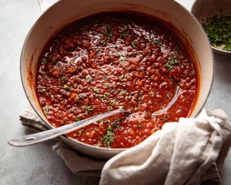 Image taken from overhead shows a pot of deep red soup with little green flecks of parsley. A ladle is sticking out of the pot.