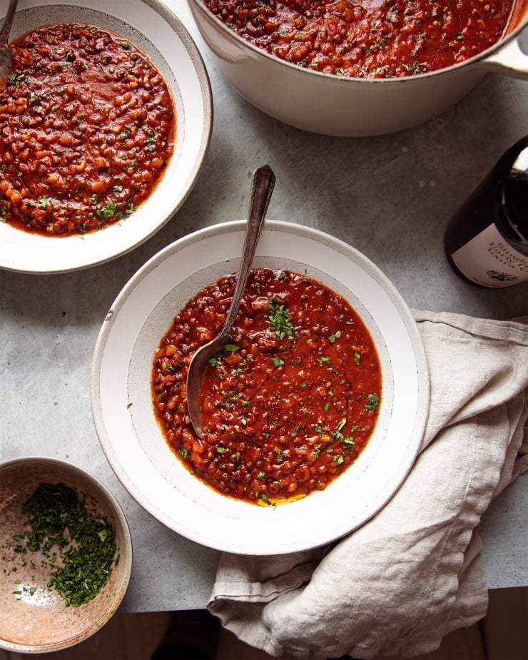 Image taken from overhead shows wide bowls of a deep red soup with little flecks of chopped parsley. A bowl of the chopped parsley is nearby.
