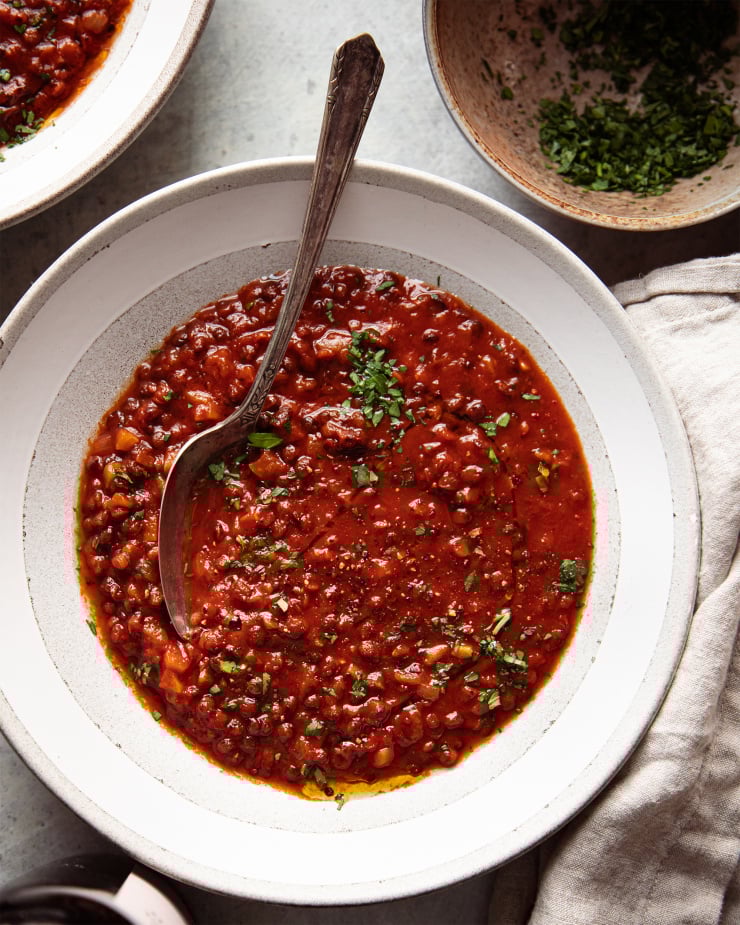 Image taken from overhead shows wide bowls of a deep red soup with little flecks of chopped parsley. A bowl of the chopped parsley is nearby.