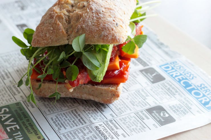 A slight 3/4 image shows an assembled vegan bbq tempeh sandwich on a multigrain roll with sprouts and avocado.