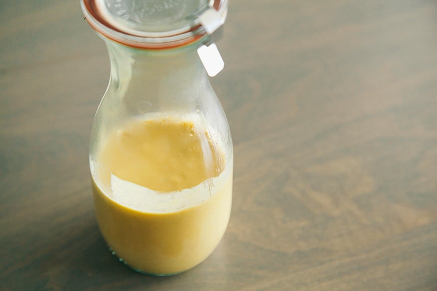 A 3/4 angle shot of some peanut sauce in a glass carafe. The carafe is on a beige-blue wood background.
