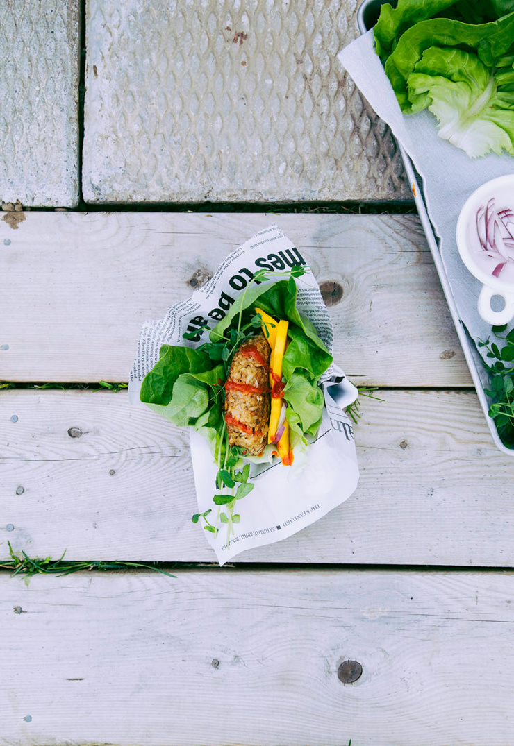 An overhead shot shows a vegan tempeh burger wrapped in lettuce on a worn wood background.