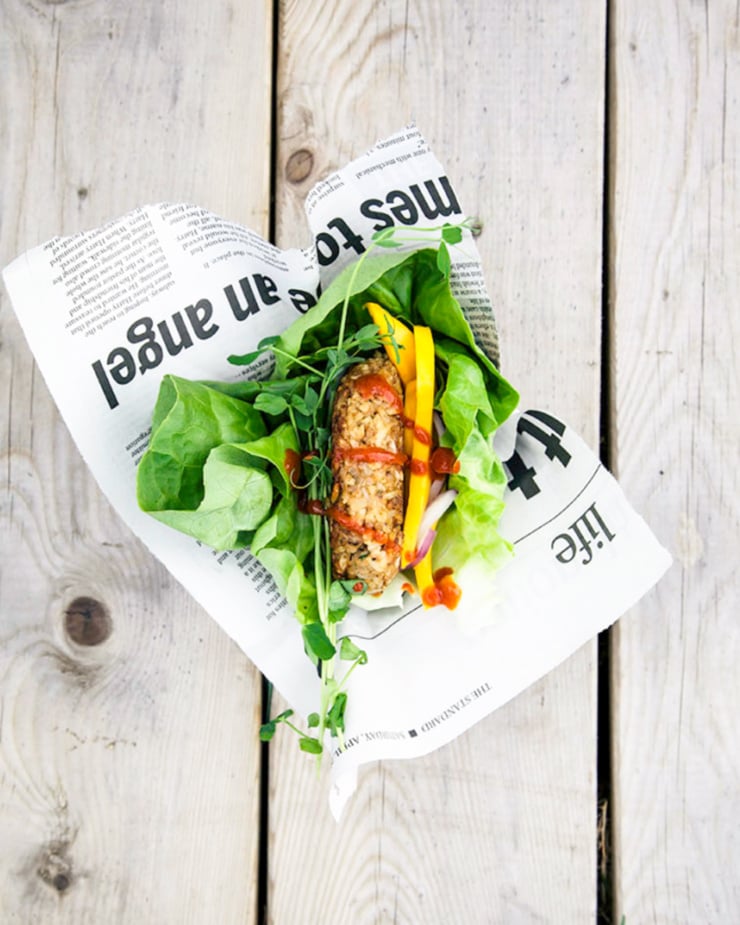 An overhead shot shows a vegan tempeh burger wrapped in lettuce on a worn wood background.