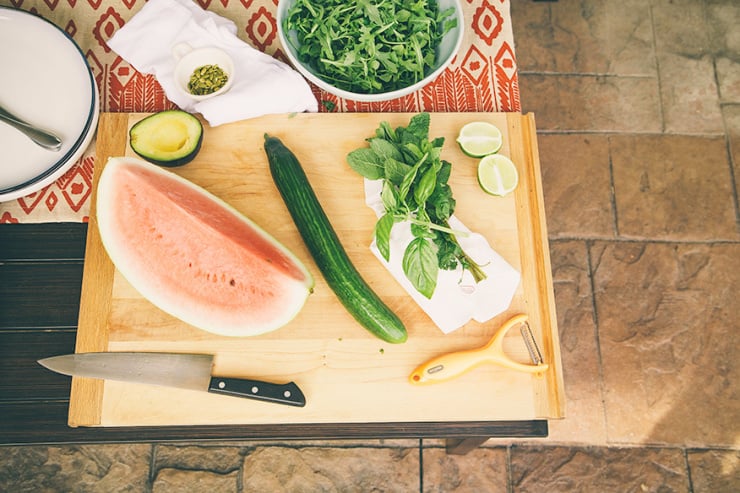 An overhead shot shows watermelon, cucumber, and herbs on a cutting board.