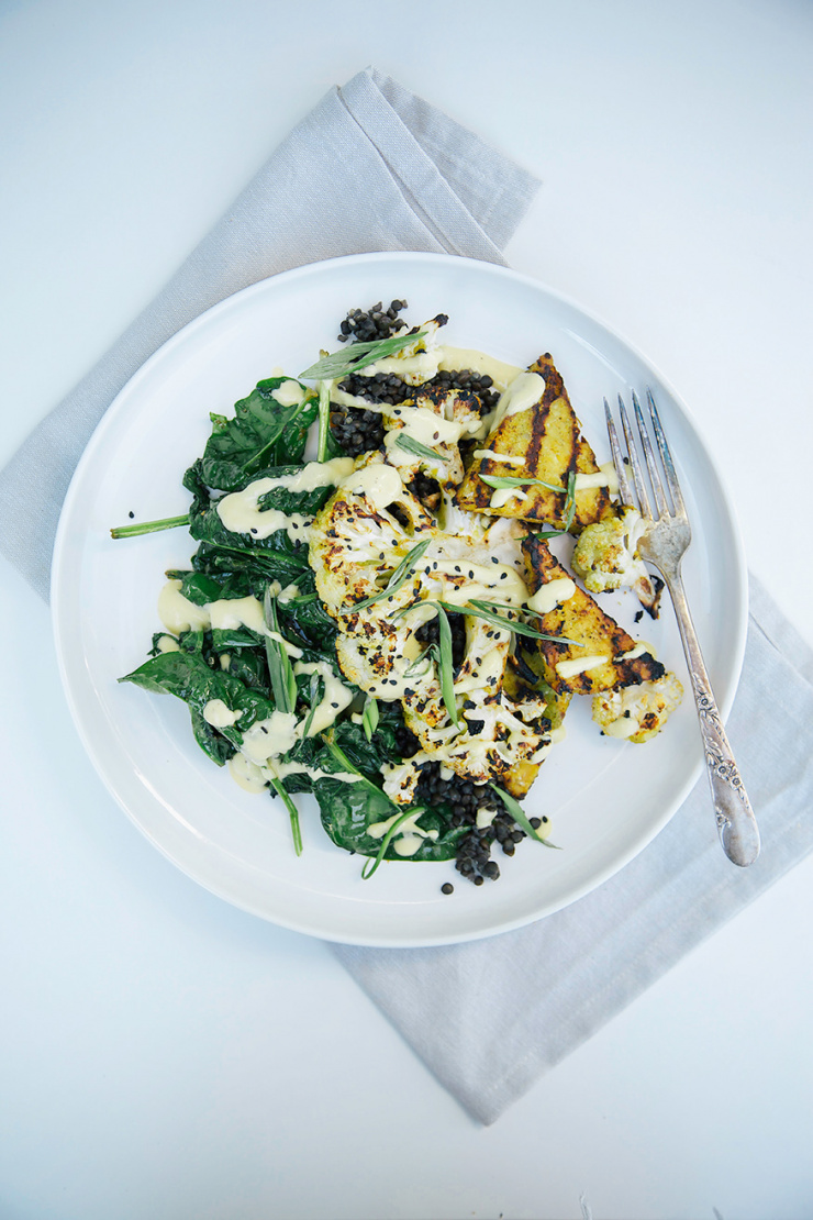 JERK-INSPIRED VEGGIE GRILL WITH MANGO GINGER SAUCE - The First Mess An overhead shot shows grilled cauliflower and tempeh and greens on a plate with lentils and a mango ginger sauce.
