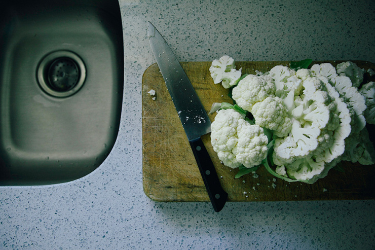 JERK-INSPIRED VEGGIE GRILL WITH MANGO GINGER SAUCE - The First Mess An overhead image shows cauliflower being cut on a board beside a sink.