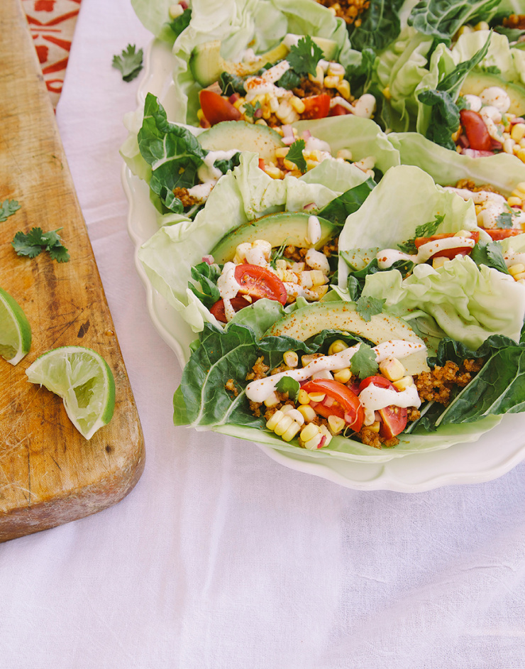 A 3/4 angle shot of a platter of raw and vegan tacos, all encased in cabbage and chard leaves.
