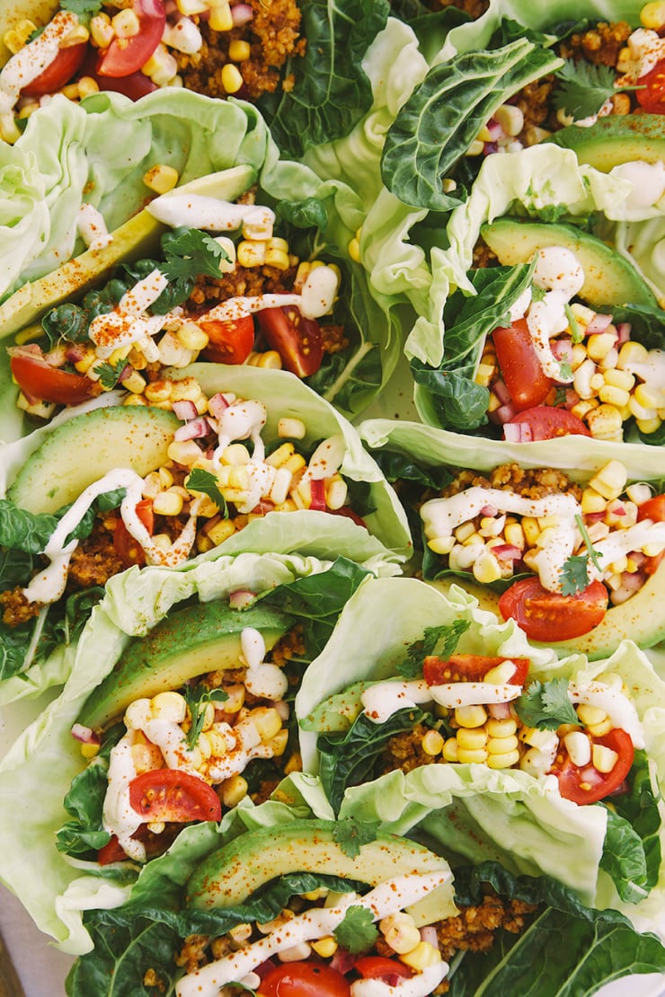An up close, overhead shot of some lettuce wraps with avocado, corn, tomatoes, ground up walnuts, and a drizzle of a creamy white sauce.