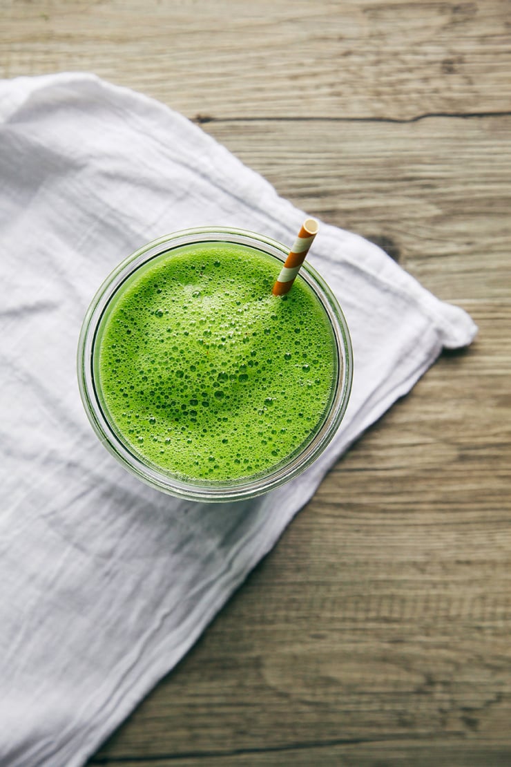 An overhead shot shows a frothy green smoothie in a glass on top of a white napkin.