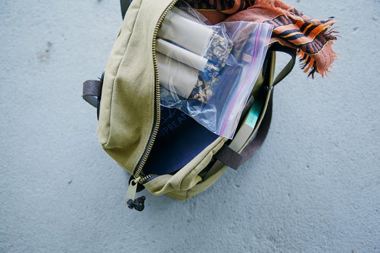 An open shoulder bag shows a scarf, bag of granola bars and a book sticking out.
