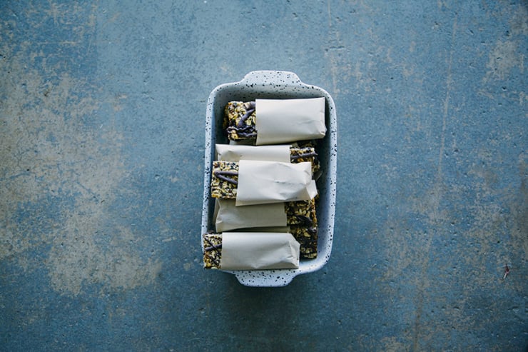 An overhead shot of wrapped banana bread granola bars in a ceramic dish on a blue stone background.