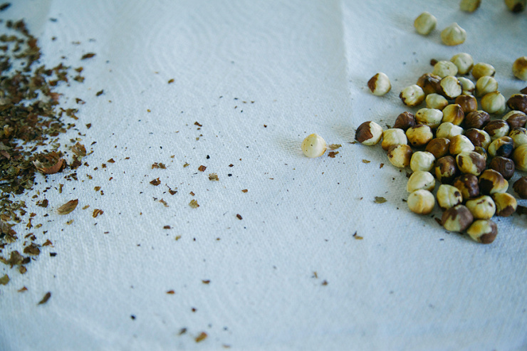A 3/4 angle shot shows toasted hazelnuts and their skins on a paper towel.