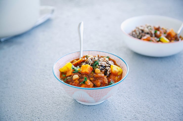 A head on shot of a chunky, deep red stew in a pink and white patterned bowl. The stew is topped with chopped green herbs.