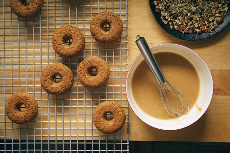 An overhead shot shows baked donuts and a small bowl of glaze nearby.