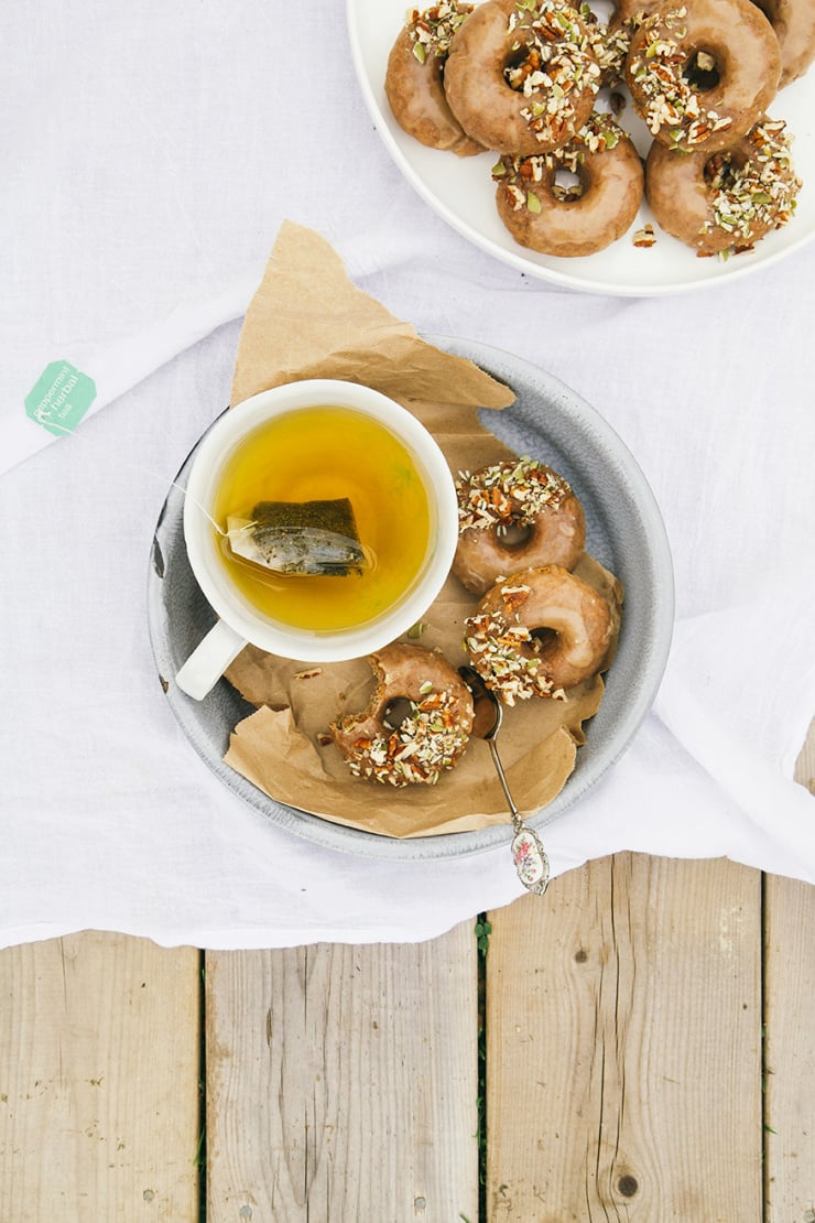 an overhead shot of a plate of small glazed donuts with a cup of tea nearby.