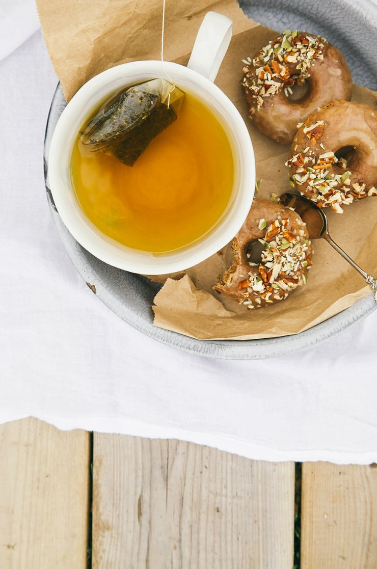 An overhead shot shows a cup of tea with 3 glazed donuts beside.