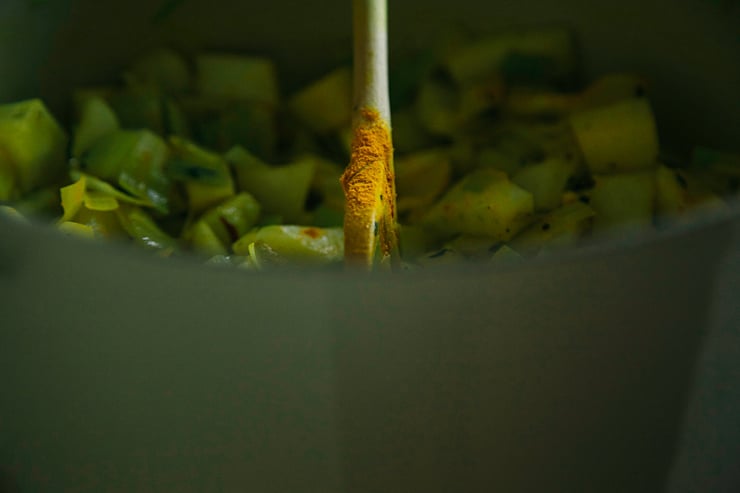 A wooden spoon is sticking out of a pot and it has a dusting of turmeric on it.