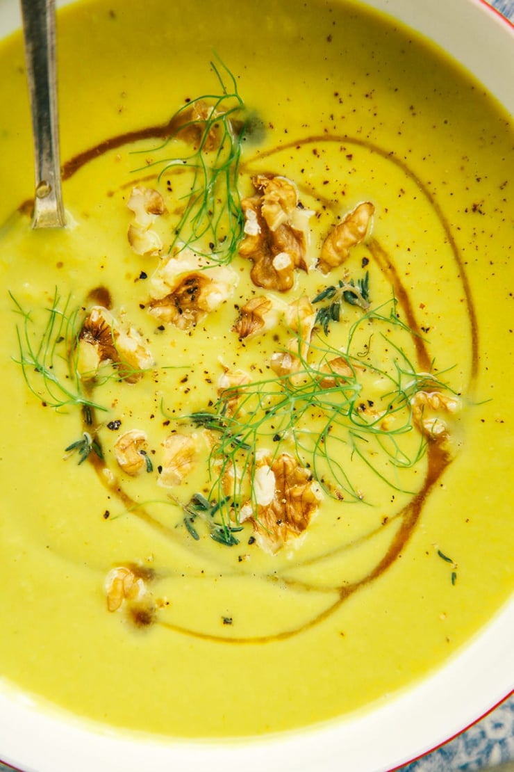 An up close, overhead shot of fennel walnut soup with leeks and turmeric. This is a puréed, golden soup that is garnished with toasted walnuts, a drizzle of maple syrup, and fennel fronds.