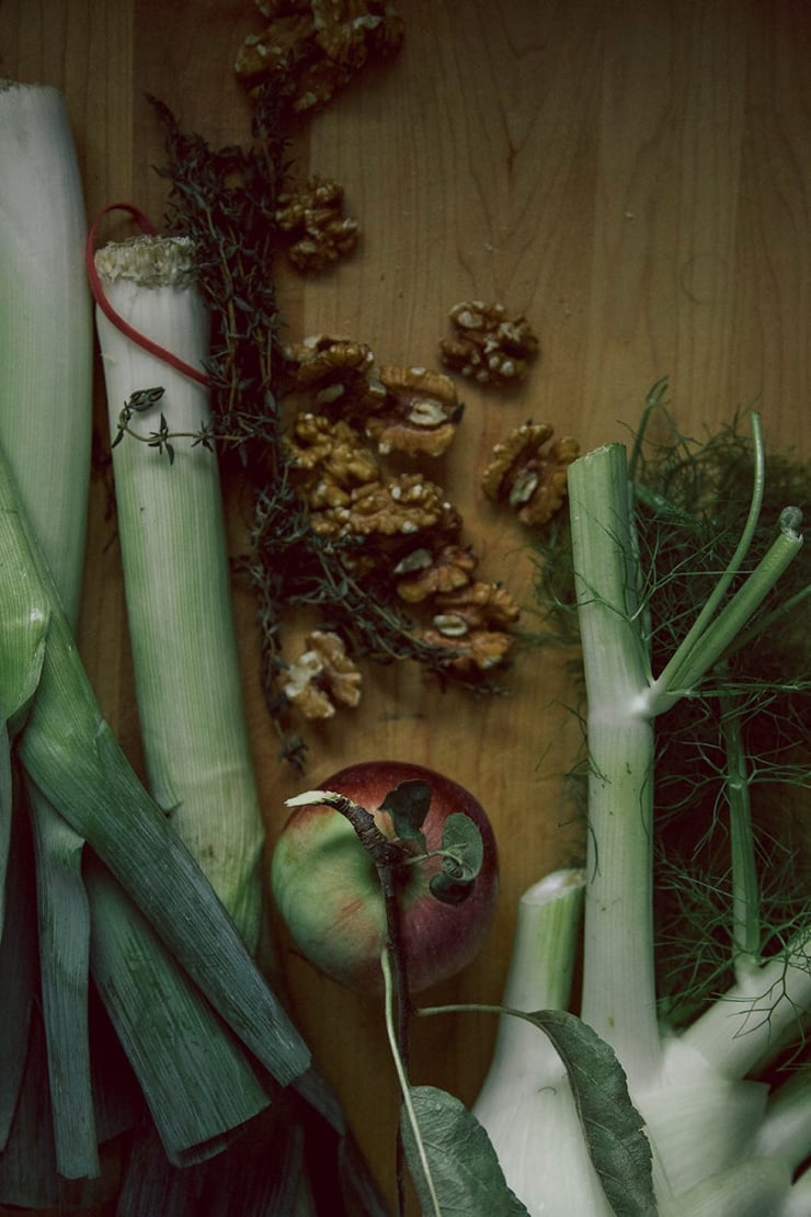 An overhead shot of soup ingredients on a light wood cutting board in moody lighting.