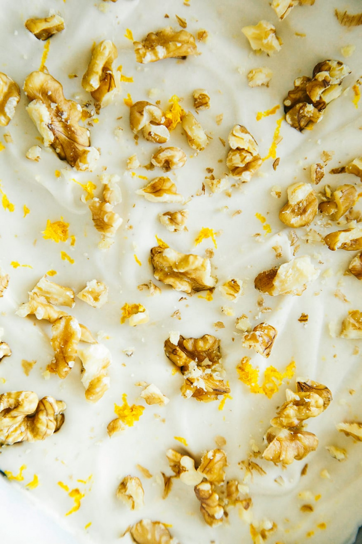 An up close shot of swooped cashew frosting topped with chopped walnuts and orange zest.