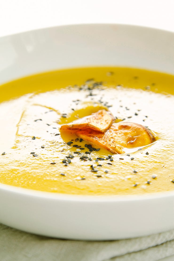 An up close, head on shot of a bowl of pureed sweet potato soup. The soup is garnished with two crispy slices of sweet potato and black sesame seeds