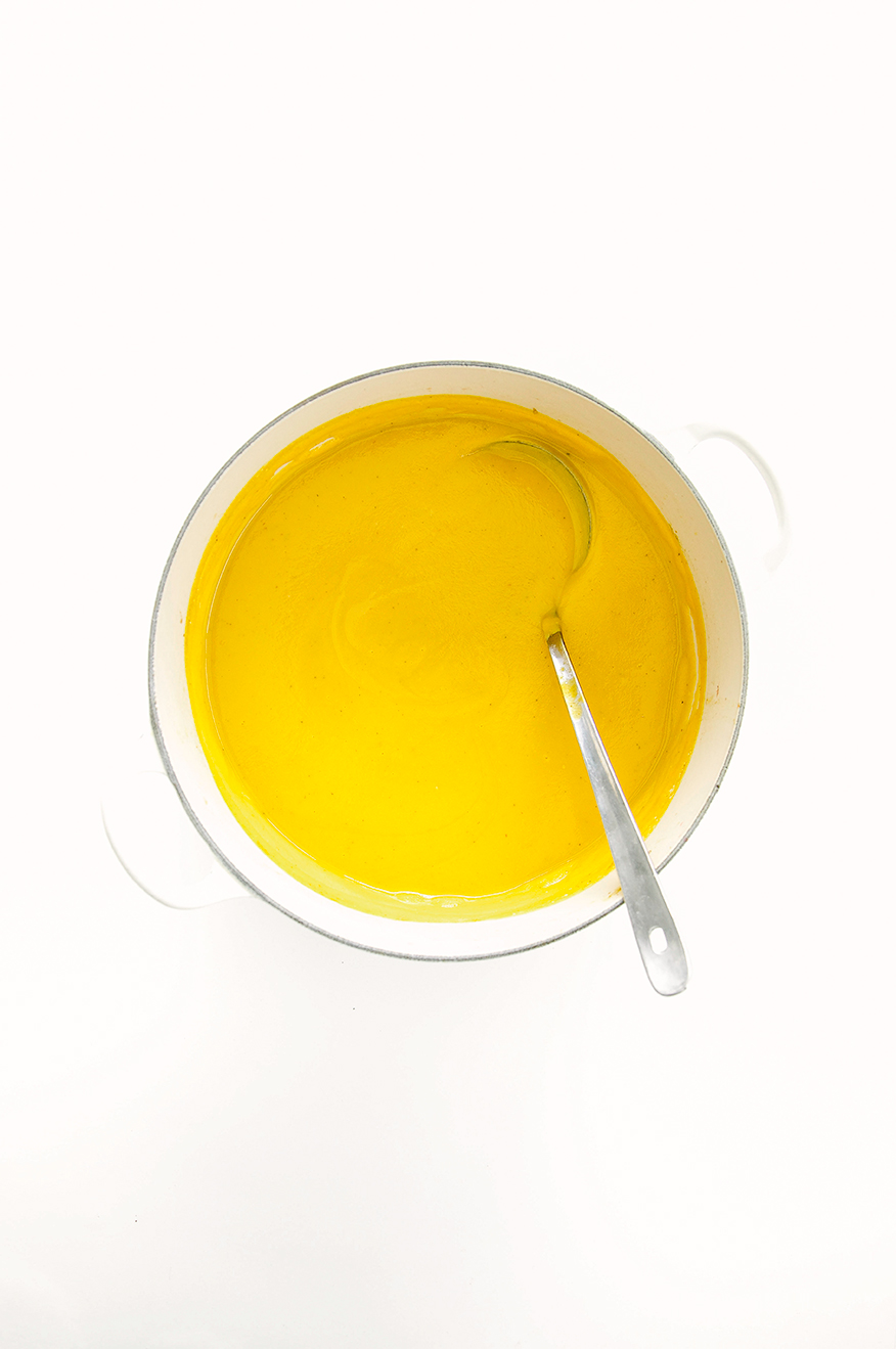An overhead shot of a creamy pureed orange-hued soup in a pot.