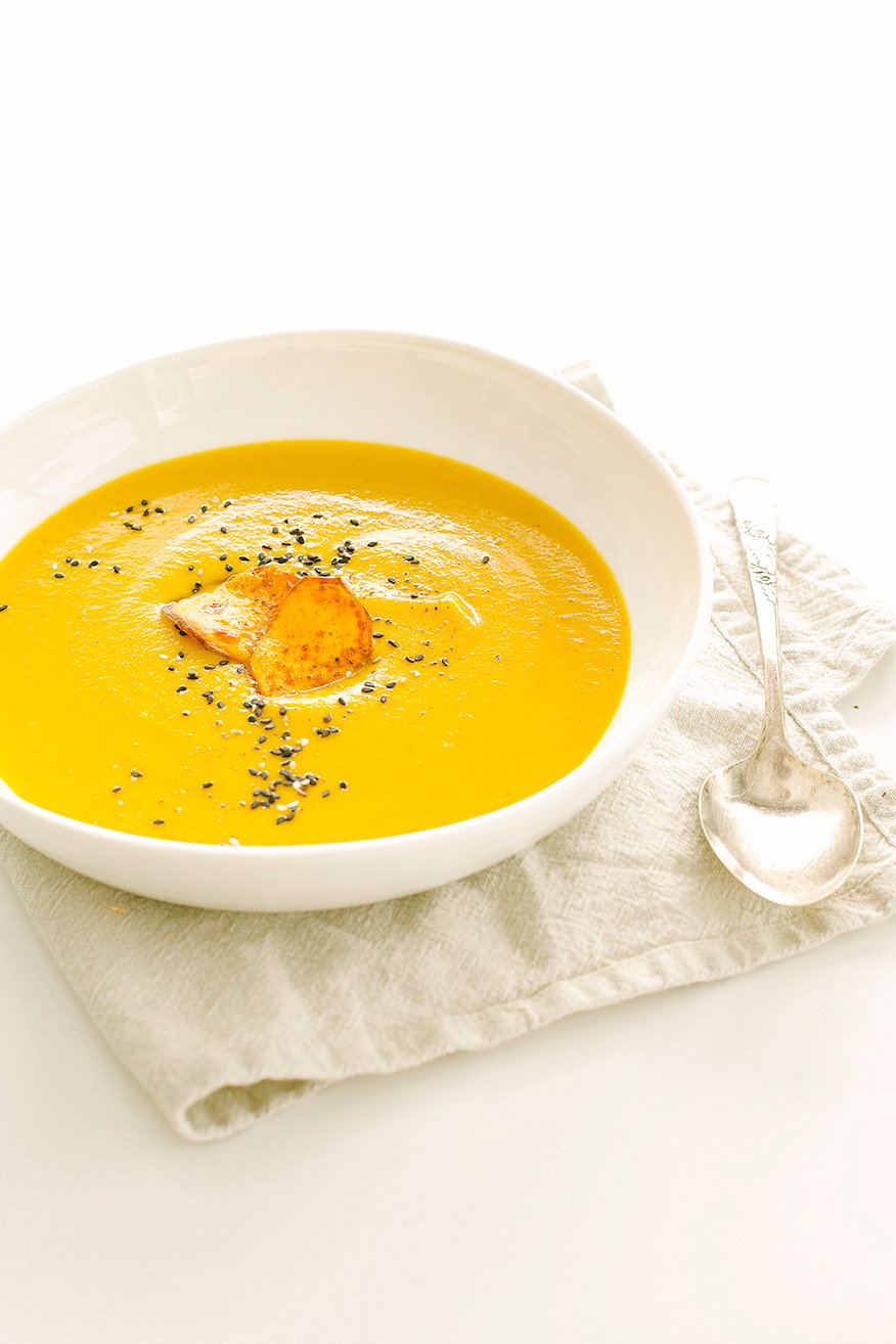 A 3/4 angle shot of a pureed sweet potato soup in a bowl. The soup is garnished with two crispy sweet potato slices and sesame seeds.
