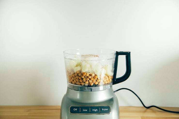 A head-on shot shows chickpeas and cauliflower in a food pprocessor.