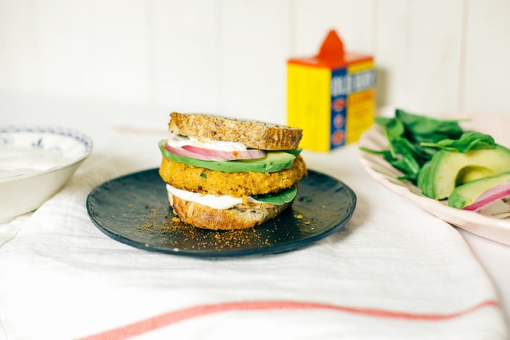 A head-on shot of a firm veggie burger with chickpeas and cauliflower. The burger is on bread and topped with avocado, red onion, and cashew mayo.
