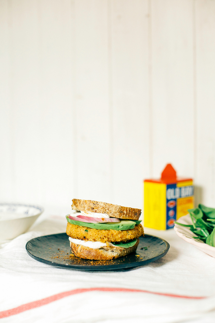A head-on shot of a firm veggie burger with chickpeas and cauliflower. The burger is on bread and topped with avocado, red onion, and cashew mayo.
