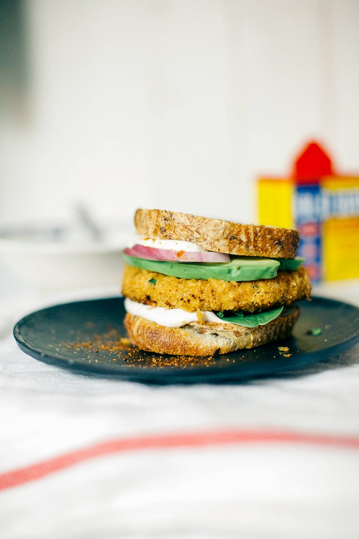 A head-on shot of a firm veggie burger with chickpeas and cauliflower. The burger is on bread and topped with avocado, red onion, and cashew mayo.