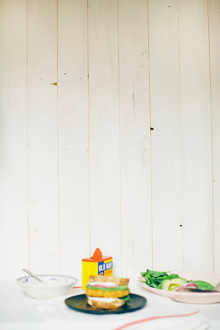 A blurry, head-on shot of a firm veggie burger with chickpeas and cauliflower. The burger is on bread and topped with avocado, red onion, and cashew mayo.