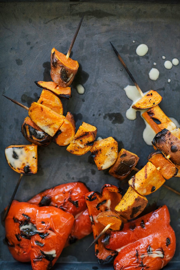 An overhead shot of grilled sweet potato pieces on skewers and grilled pieces of red bell pepper.