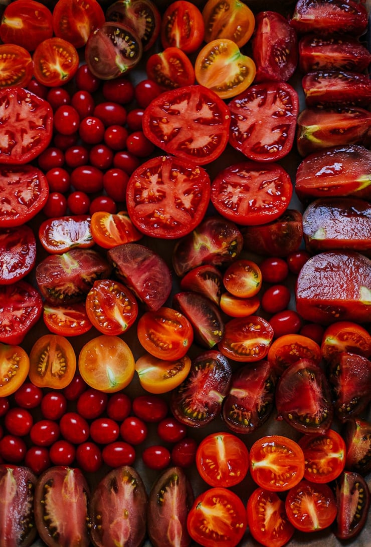 An overhead shot of a bunch of cut heirloom tomatoes on a sheet pan, just before being roasted.