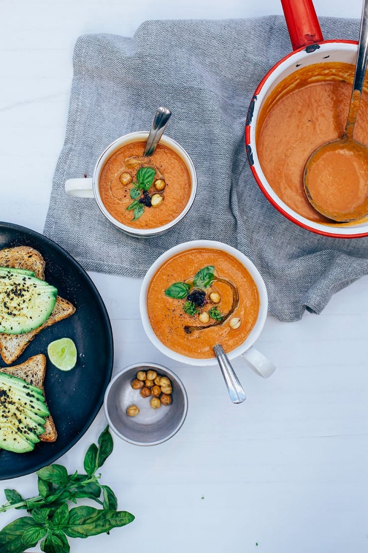 Overhead shot of creamy vegan tomato soup, served in mugs with some crispy chickpeas as garnish.