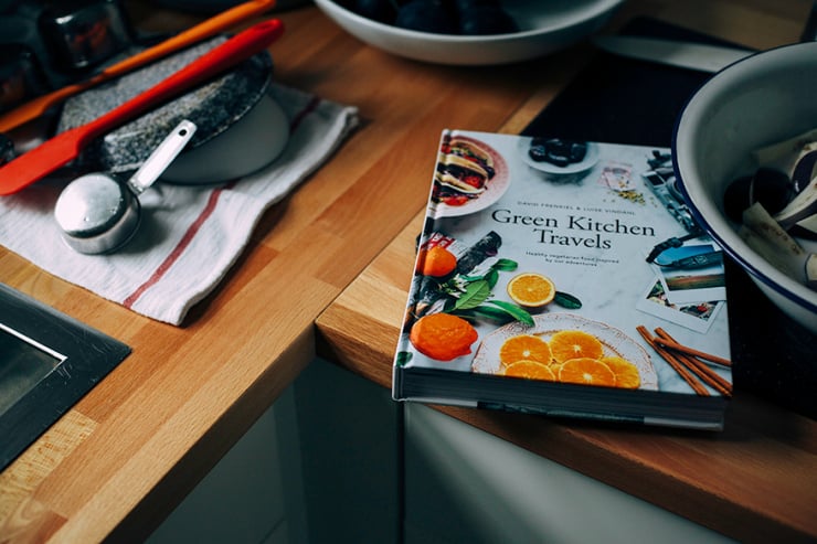 A 3/4 angle shot of the book Green Kitchen Travels on a wood countertop.