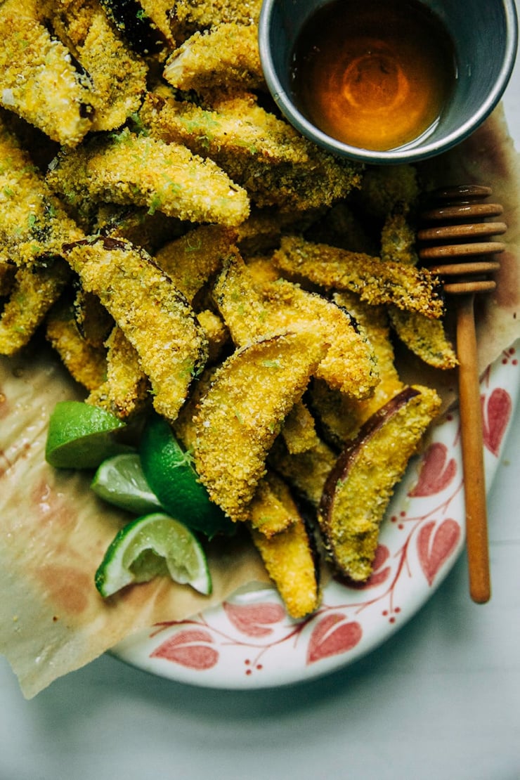 An overhead shot of polenta-coated slices of eggplant with wedges of lime and a little container of agave nectar to the side.
