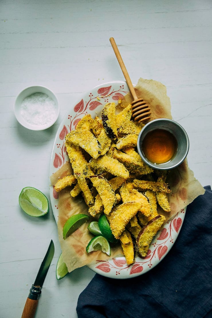 an overhead shot of crispy eggplant polenta fries with honey and lime wedges to the side.