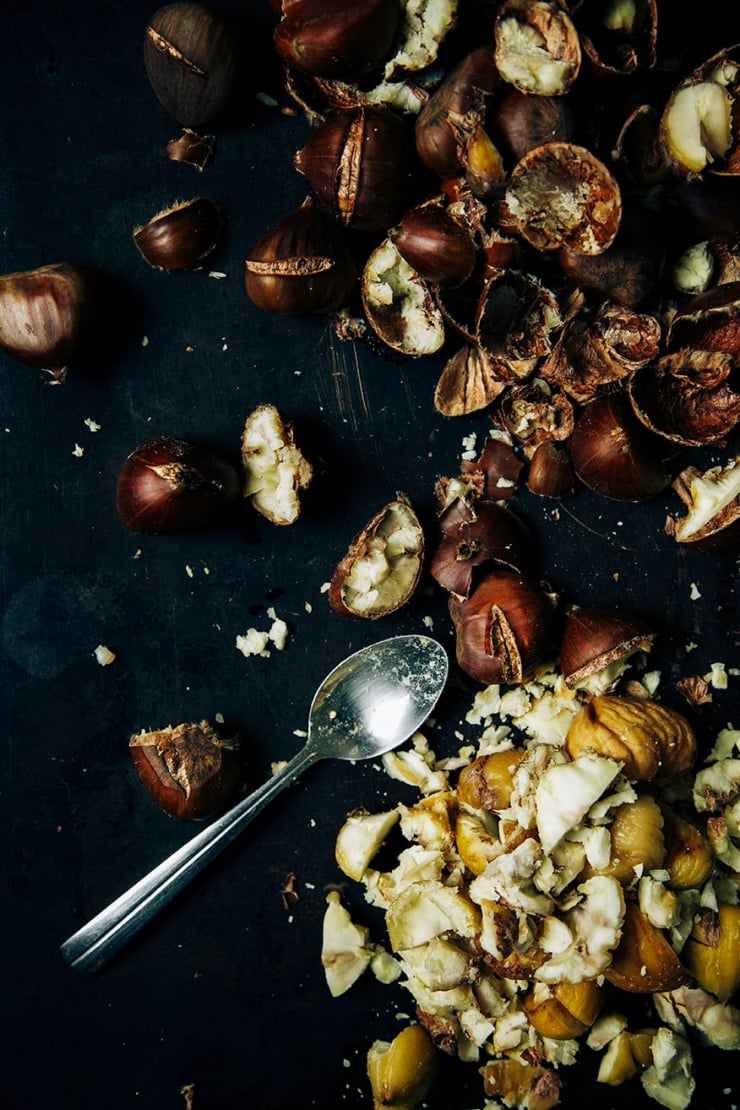 An overhead shot of roasted and peeled chestnuts on a black metal sheet pan.