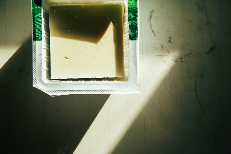 An overhead shot of a package of firm tofu in harsh, partially shadowed light. The package is peeled open.