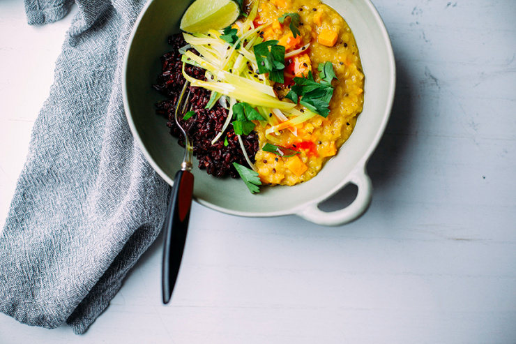 An overhead shot of a creamy orange stew with cooked black rice and a wedge of lime to the side. The stew is topped with cooked leeks and photographed in a light green bowl.