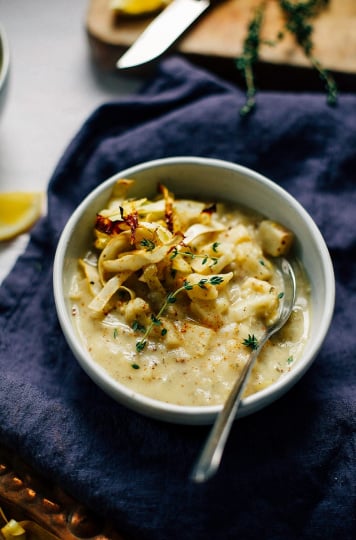 A 3/4 shot of a winter vegetable chowder in a white bowl. The chowder is creamy coloured and topped with crispy roasted strips of cabbage. The bowl is perched on top of a deep blue napkin on top of a white background.