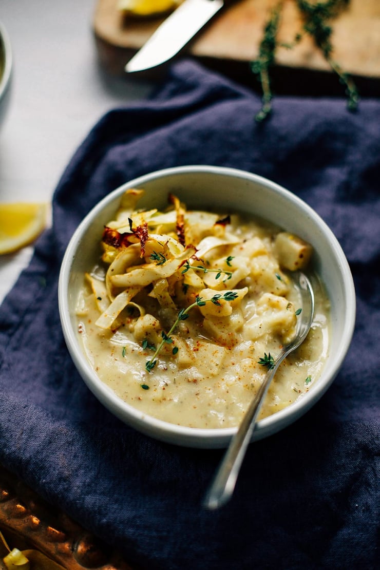 A 3/4 shot of a winter vegetable chowder in a white bowl. The chowder is creamy coloured and topped with crispy roasted strips of cabbage. The bowl is perched on top of a deep blue napkin on top of a white background.