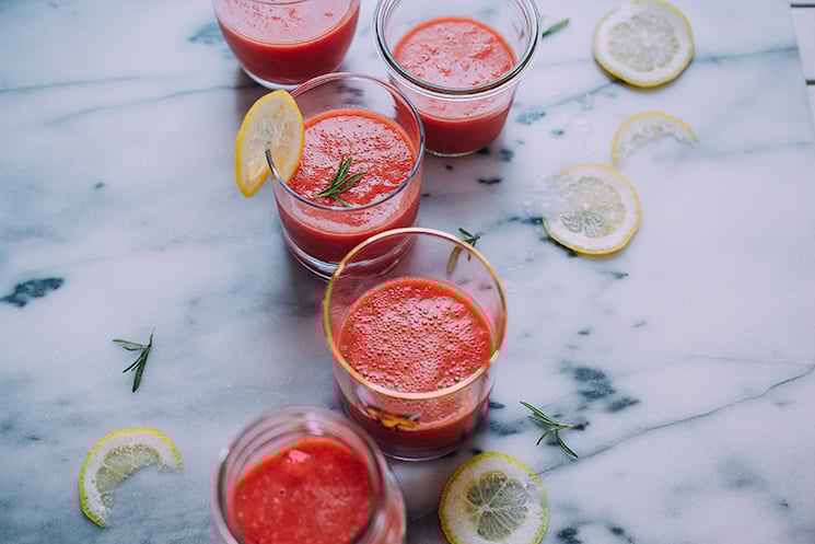 An overhead shot of bright pink frozen watermelon-ade in 5 different, clear glasses. Glasses are filled at the halfway mark and are on top of a marble background.