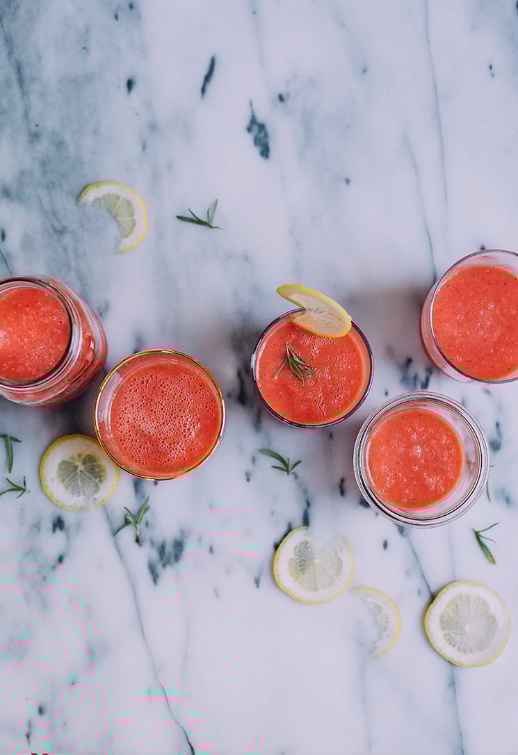 An overhead shot of bright pink frozen watermelon-ade in 5 different, clear glasses. Glasses are filled at the halfway mark and are on top of a marble background.