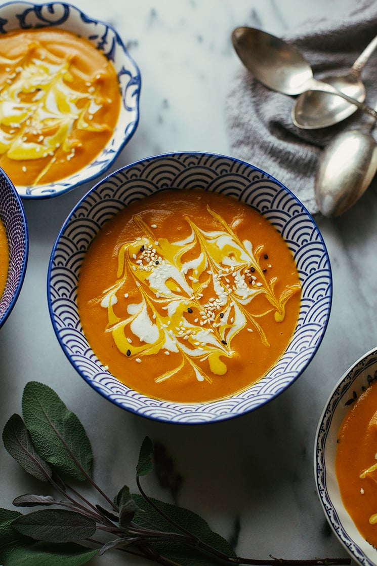 An overhead shot of bright orange ginger carrot bisque soup in a patterned blue and white bowl on a grey marble background.