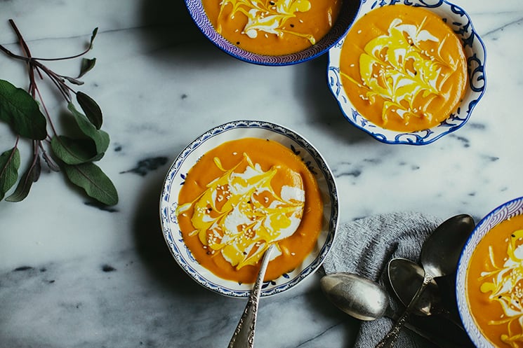 An overhead shot of bright orange ginger carrot bisque soup in 4 patterned blue and white bowls on a grey marble background.
