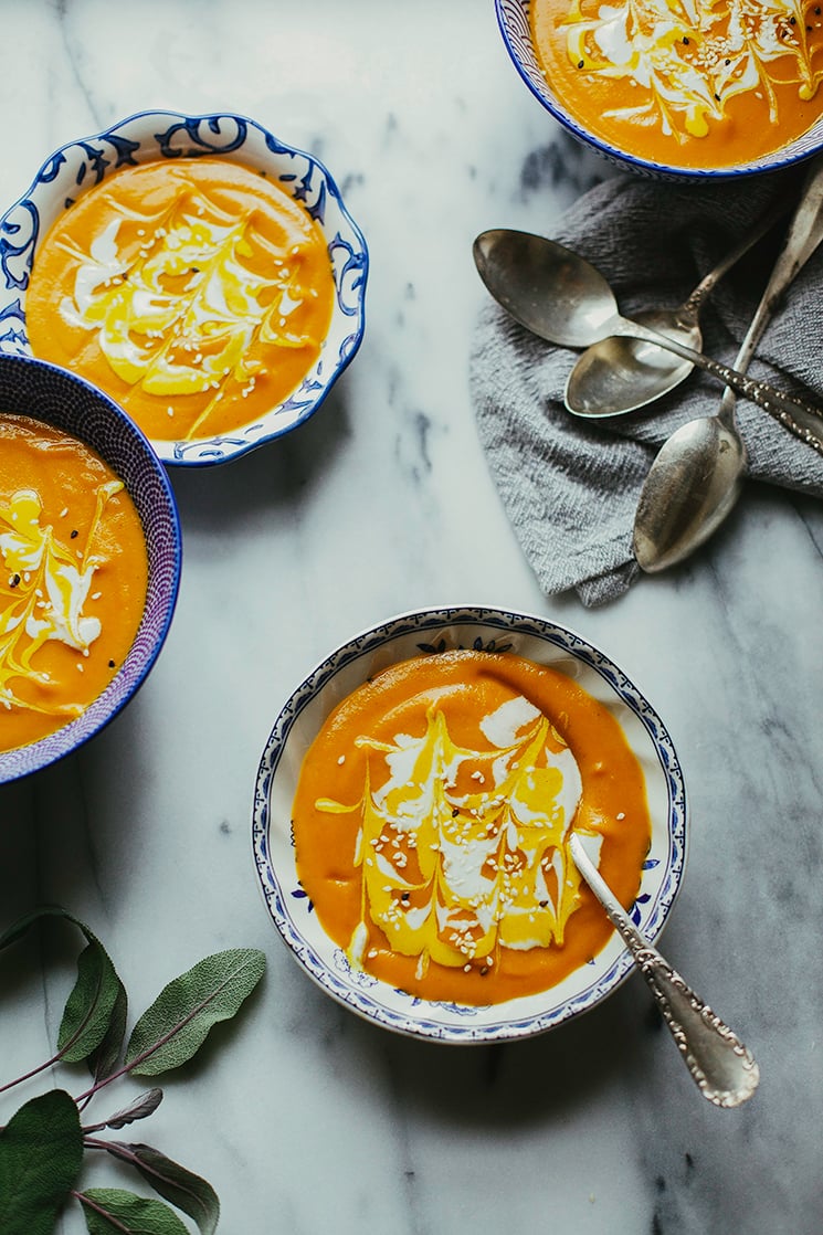 An overhead shot of bright orange ginger carrot bisque soup in 4 patterned blue and white bowls on a grey marble background.